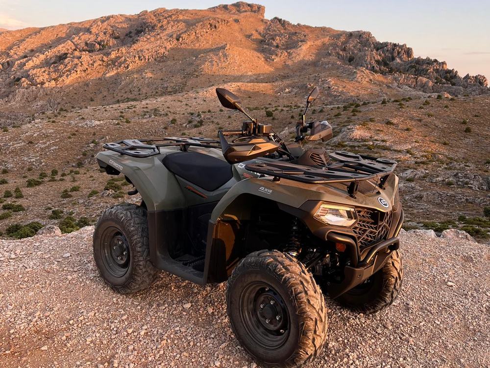 Quad CFMOTO 4x4 verde oliva su sterrato di ghiaia, con montagna calcarea e macchia bassa nella luce calda del tramonto